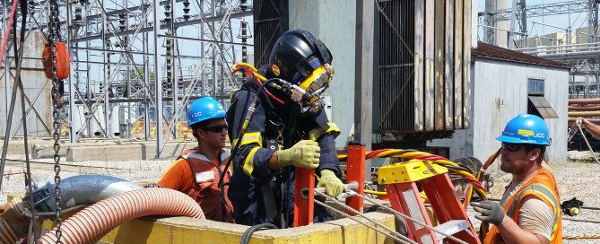 Underwater Construction Corporation diver in diving gear lowering by ladder into an intake bay at a fossil fuel plant.
