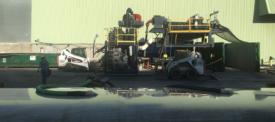 geotube-processing A large Geotube dewatering system in operation, with two Bobcat skid-steer loaders nearby at a jobsite managed by UCC.
